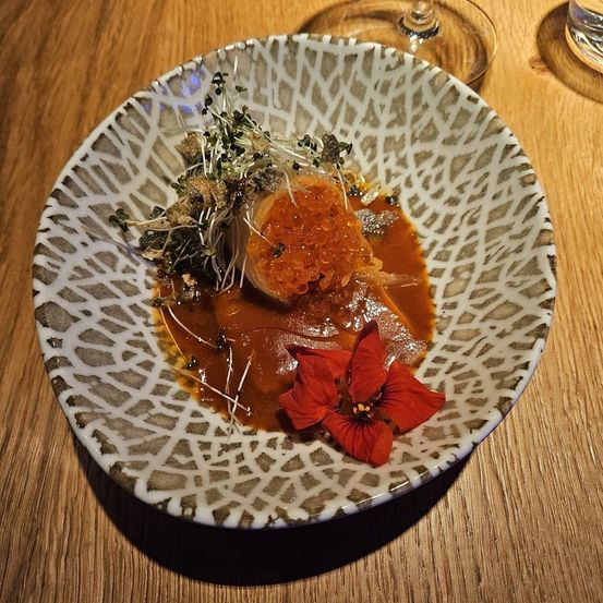 Ein Gericht mit roter Sauce und einer roten Blume auf einem gemusterten Teller auf einem Holztisch.
