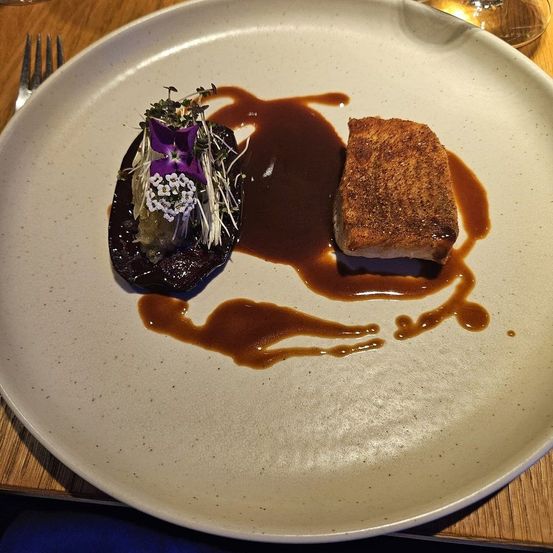 Ein weißer Teller mit einem gebratenen Gemüse- und Fleischgericht, mit brauner Sauce beträufelt und mit Blumen garniert.