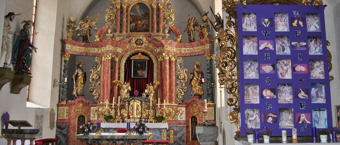 Das Innere einer Kirche mit einem goldenen und roten Altar, Statuen, einem gerahmten Gemälde und einem violetten gerahmten Bild mit den Buchstaben WEG E.