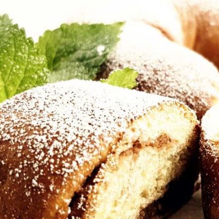 Ein Nahaufnahme eines Kuchenstücks mit Puderzucker darauf, ein Minzblatt daneben und ein unscharfer Hintergrund.