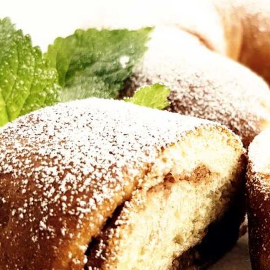 Ein Nahaufnahme eines Kuchenstücks mit Puderzucker darauf, ein Minzblatt daneben und ein unscharfer Hintergrund.