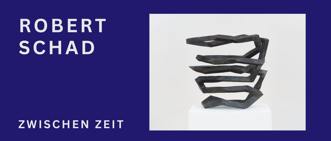 Eine moderne abstrakte Skulptur aus Metall mit geometrischem Design, auf einem weißen Sockel vor blauem Hintergrund ausgestellt.