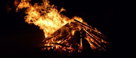 Ein Lagerfeuer brennt in der dunklen Nacht intensiv, mit aufsteigenden Flammen und knisterndem Holz.