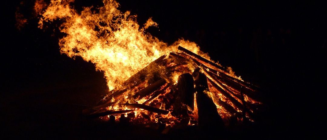 Ein Lagerfeuer brennt in der dunklen Nacht intensiv, mit aufsteigenden Flammen und knisterndem Holz.