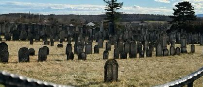 Ein Friedhof mit vielen Grabsteinen und einem Zaun, vor dem Hintergrund von Bergen und einem klaren Himmel.