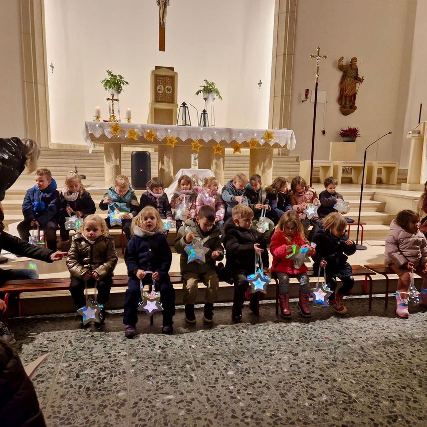 Kinder sitzen in einer Kirche, halten sternförmige Dekorationen in der Hand, mit einem Altar und einer Statue im Hintergrund.