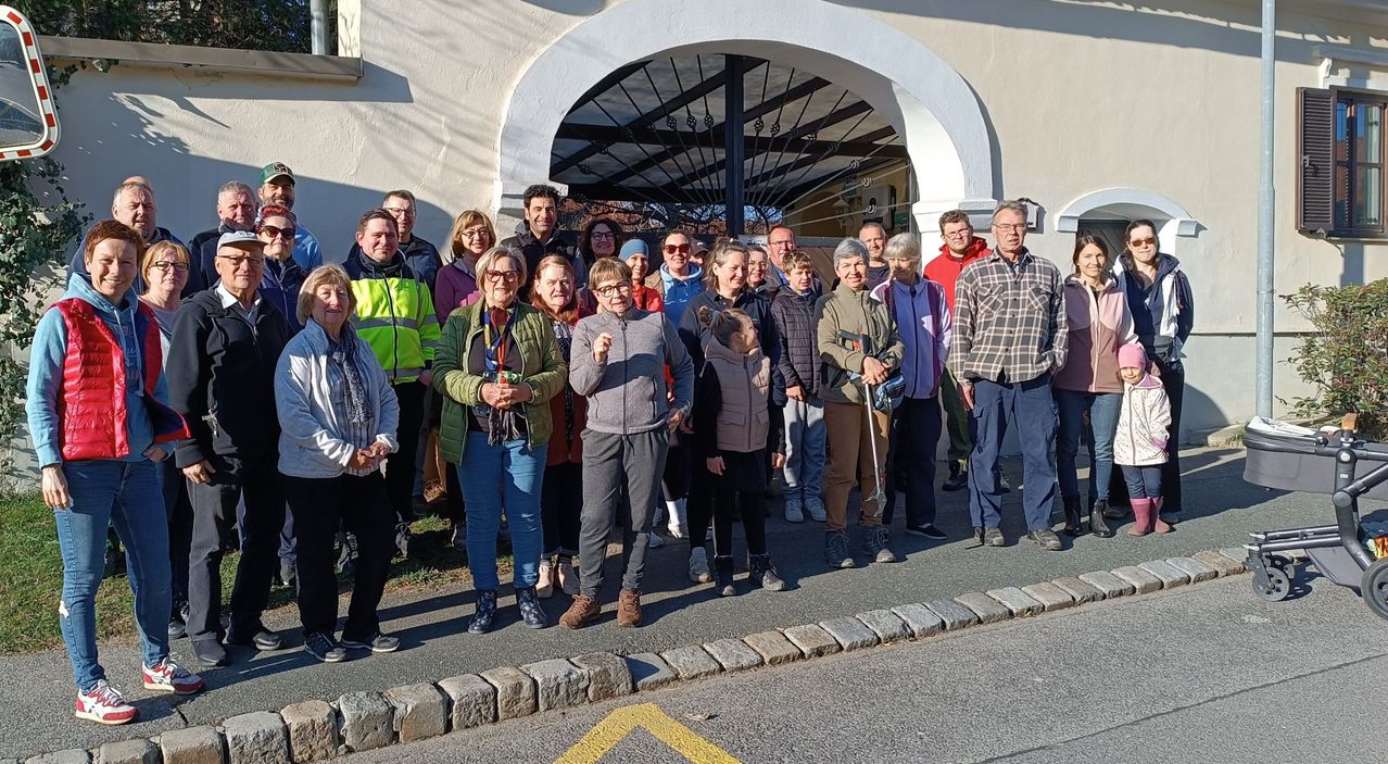 Eine Gruppe von Menschen steht draußen vor einem Gebäude mit einem gewölbten Eingang. Sie lächeln und scheinen für ein Foto zu posieren.