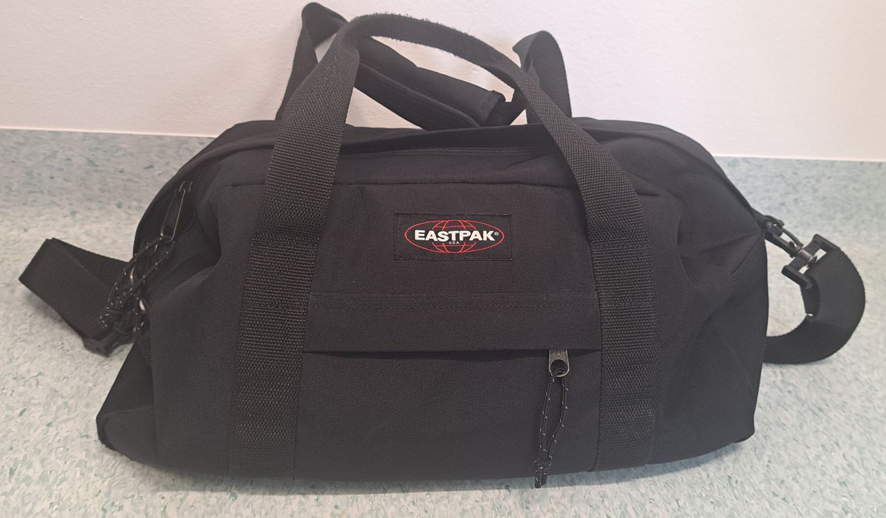 Eine schwarze Eastpak-Tasche mit rotem Logo und Reißverschluss. Die Tasche steht auf einer weißen Oberfläche.