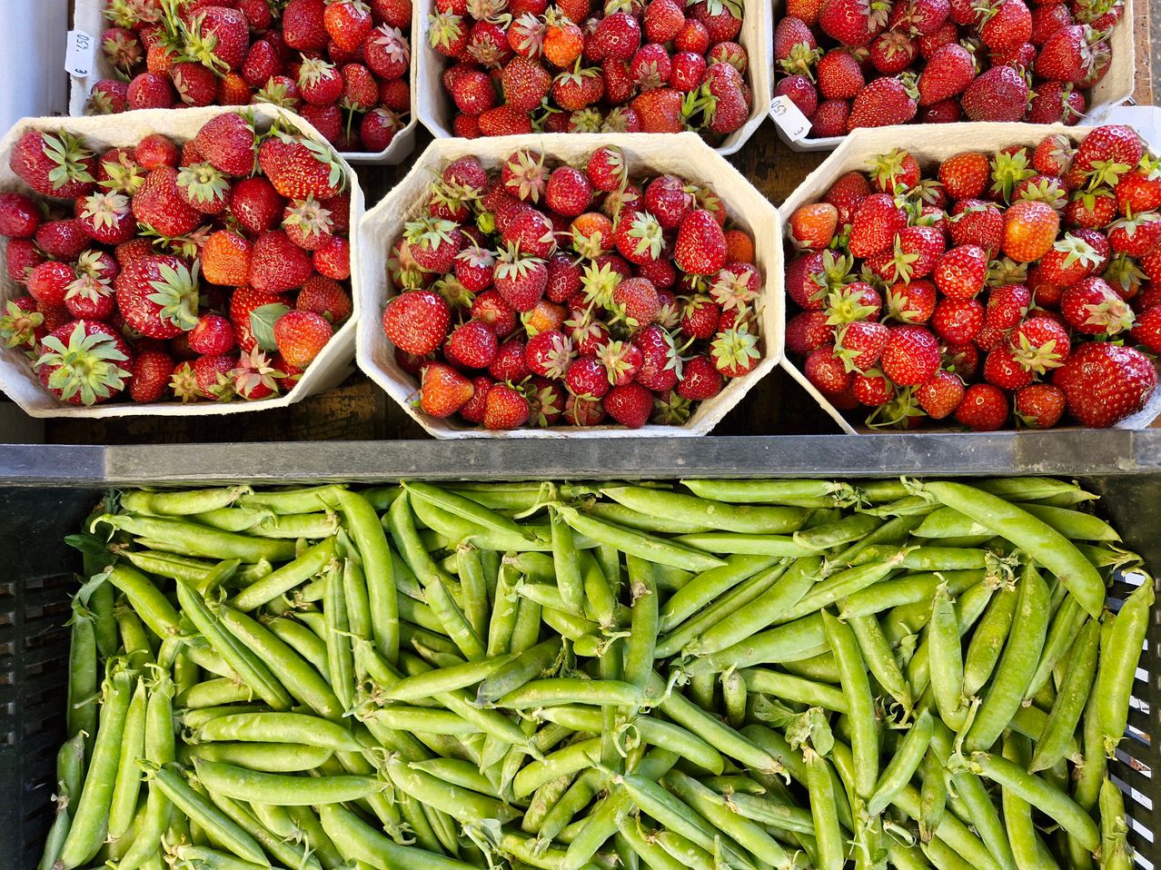 Eine Ausstellung von Erdbeeren in weißen Körben über einem großen Haufen grüner Erbsen.