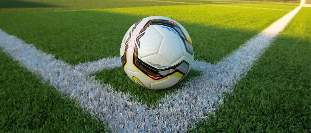 Ein Fußball liegt auf einem Rasenfeld in der Nähe der weißen Begrenzungslinie und ist bereit für ein Spiel.