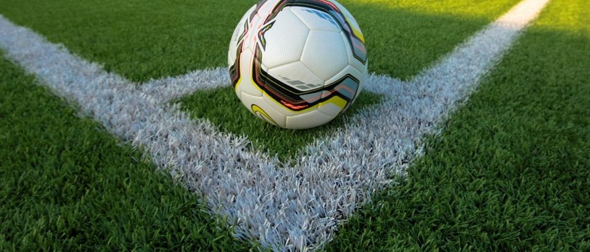 Ein Fußball liegt auf einem Rasenfeld mit weißen Linien, die die Grenzen markieren. Der Ball ist weiß mit schwarzen und roten Akzenten.
