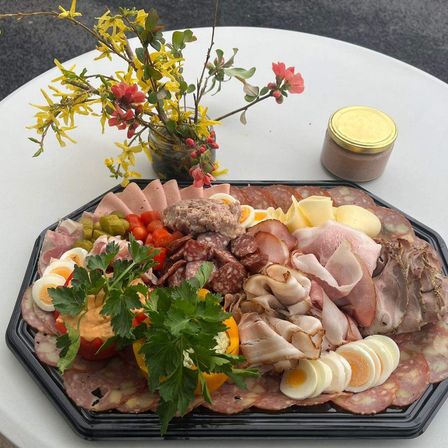 Ein Tablett mit verschiedenen Fleischsorten, Käse und Gemüse, mit Blumen garniert, auf einem weißen Tisch platziert.