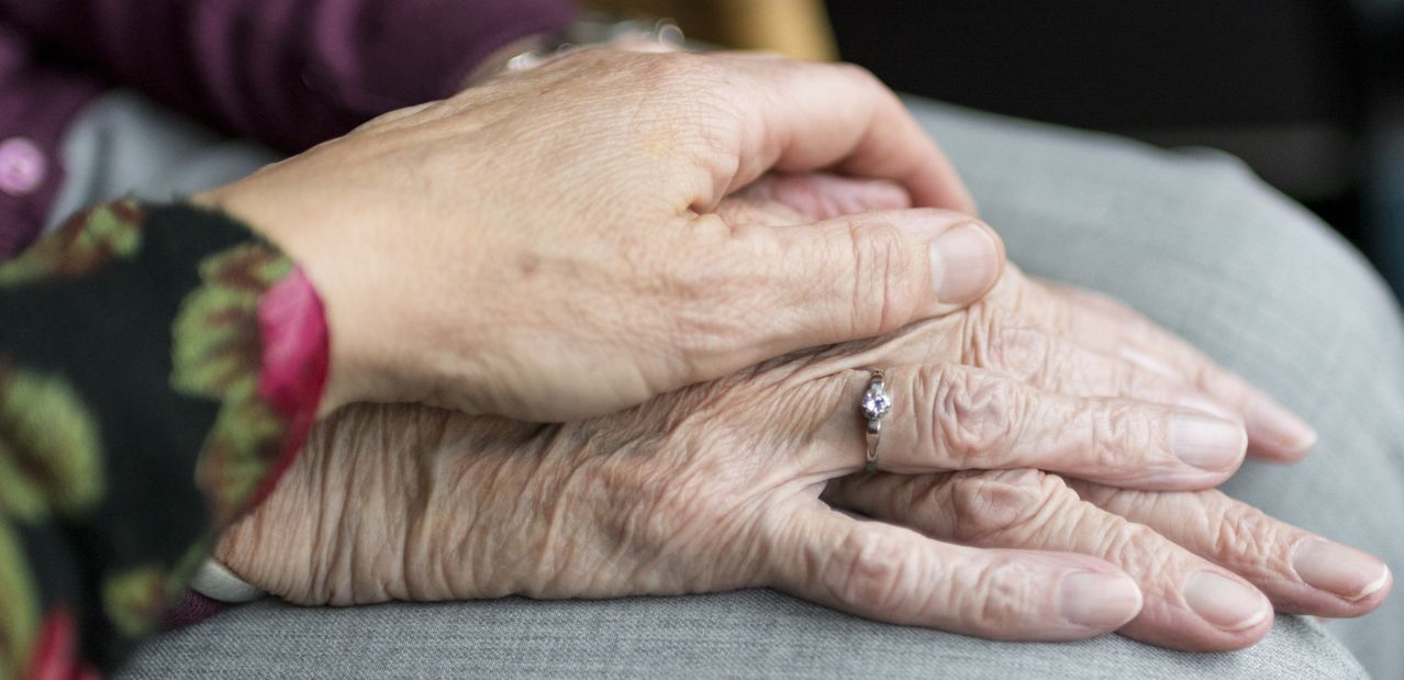 Nahaufnahme von älteren Händen, die sich halten, eine Hand mit einem Ehering mit einem kleinen Diamanten.