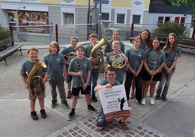 Eine Gruppe von Kindern und ein Erwachsener posieren mit Musikinstrumenten vor einem Gebäude. Der Erwachsene hält ein Schild mit einem Bild eines Golfers.