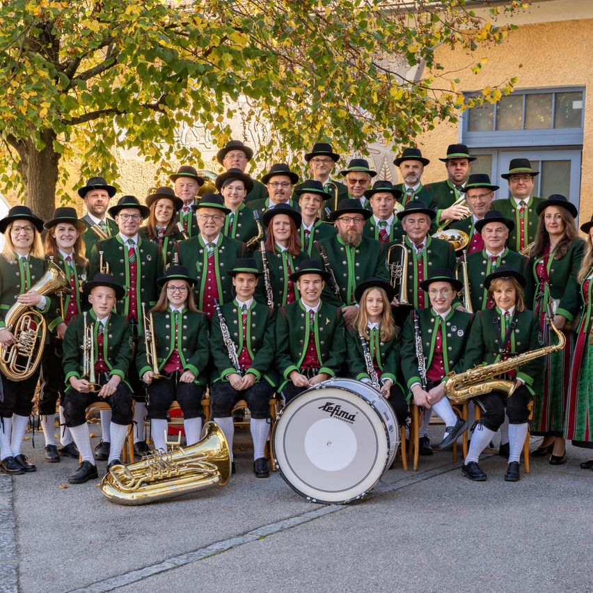 Eine Musikkapelle in traditioneller deutscher Kleidung mit Blech- und Holzblasinstrumenten posiert für ein Foto vor einem Gebäude.