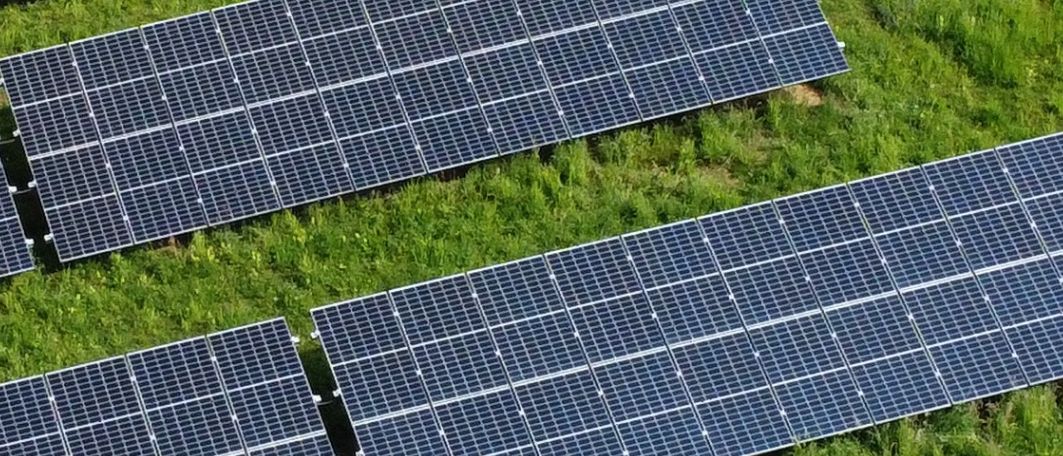 Eine Luftaufnahme eines grasigen Feldes mit mehreren installierten Solarmodulen, umgeben von Bäumen und einer Straße.