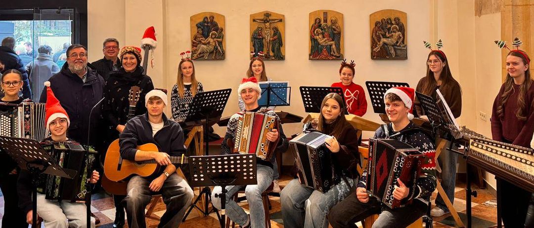 Eine Gruppe von Musikern in Weihnachtsmützen und Pullovern spielt verschiedene Instrumente in einer Kirche.