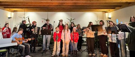 A group of people are performing on a stage with various musical instruments. The stage is decorated with Christmas trees.