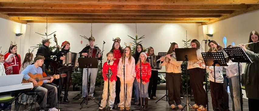 Eine Gruppe von Menschen tritt mit verschiedenen Musikinstrumenten auf einer Bühne auf. Die Bühne ist mit Weihnachtsbäumen geschmückt.
