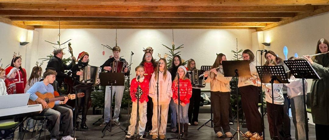 Eine Gruppe von Menschen tritt mit verschiedenen Musikinstrumenten auf einer Bühne auf. Die Bühne ist mit Weihnachtsbäumen geschmückt.