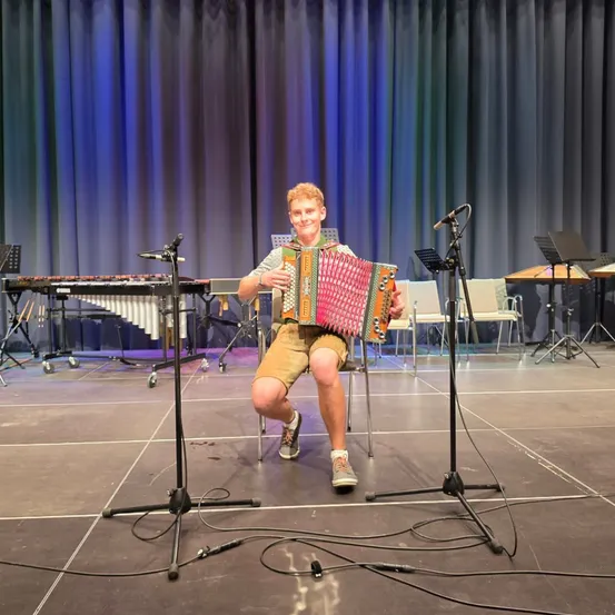 Ein junger Mann spielt Akkordeon auf der Bühne, mit Mikrofonen und Musikinstrumenten im Hintergrund.