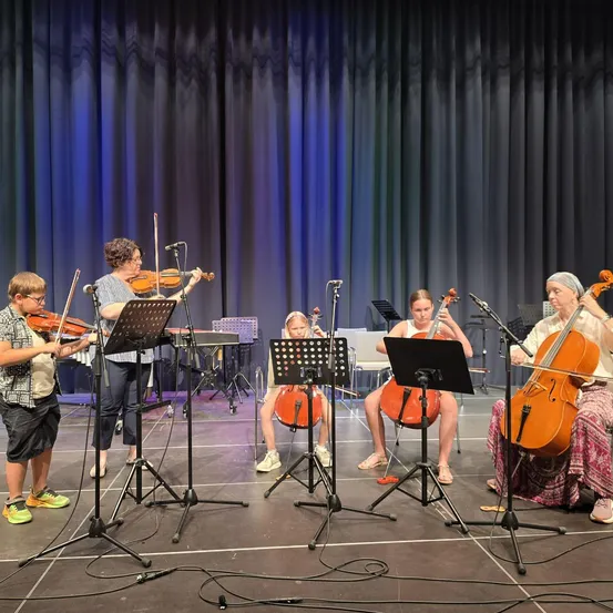 Fünf Musiker, darunter ein junger Junge, spielen auf der Bühne mit Violinen und Celli vor einem blauen Vorhang.
