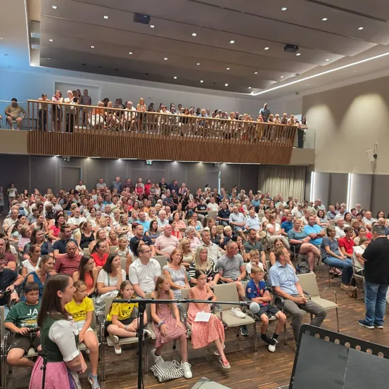 Eine große Menschenmenge sitzt in einem Auditorium, einige stehen auf der Galerie, mit einer Frau, die vor einem Mikrofon auf einem Ständer steht.