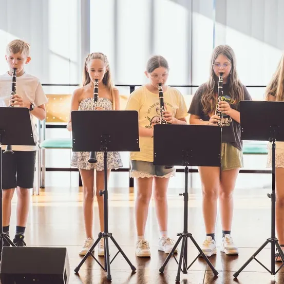 Fünf Kinder stehen in einer Reihe, jedes hält eine Klarinette und scheint eine musikalische Aufführung zu proben.