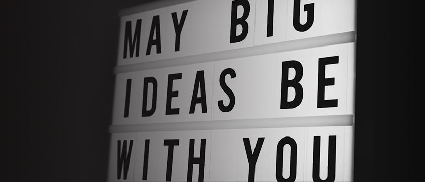 Ein weißes Schild zeigt den Satz 'Mögen große Ideen mit dir sein' in fetten schwarzen Buchstaben. Das Schild ist in drei horizontale Abschnitte unterteilt.
