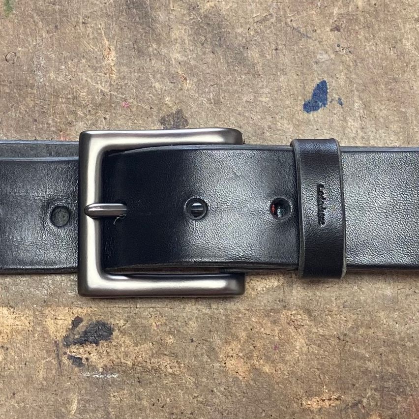 Ein Nahaufnahme eines schwarzen Ledergürtels mit einer silbernen Schnalle und einem schwarzen Lederriemen liegt auf einer Holzoberfläche.