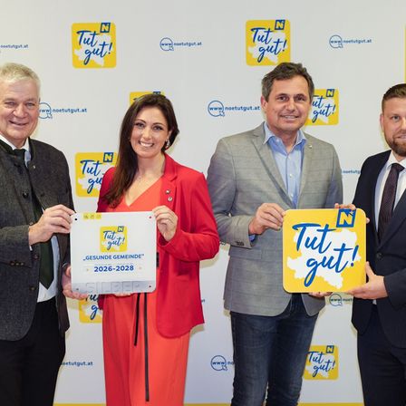 Vier Personen stehen mit Plakaten posierend, zwei halten weiße Zertifikate und zwei halten gelbe Plakate. Sie alle lächeln für ein Foto.
