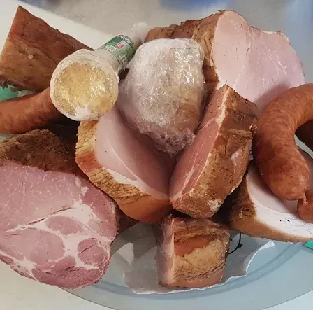 Ein Teller mit verschiedenen Fleischsorten, darunter Würste, Schinken und andere Stücke, einige in Plastik eingewickelt.