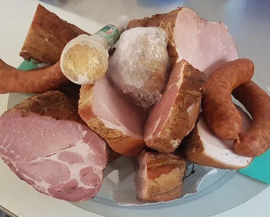 Ein Teller mit verschiedenen Fleischsorten, darunter Würste, Schinken und andere Stücke, einige in Plastik eingewickelt.