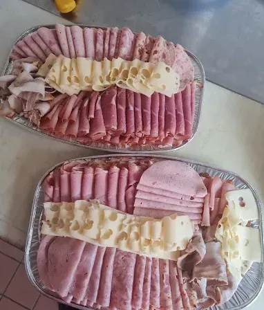Zwei Tabletts mit verschiedenen Fleisch- und Käsesorten auf einer gefliesten Oberfläche. Das obere Tablett hat geschnittenen Schinken, Käse und andere Fleischsorten. Das untere Tablett hat Scheiben von Schinken, Käse und anderen Fleischsorten.