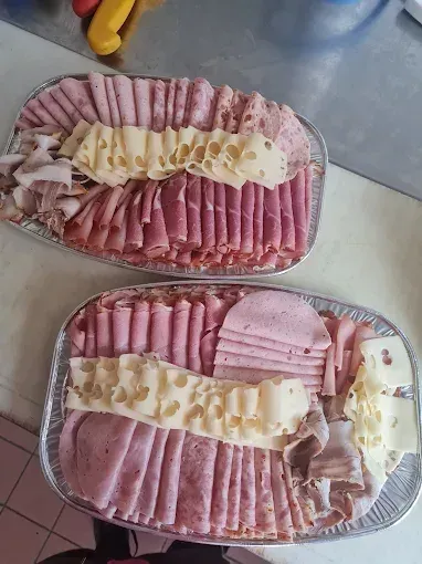 Zwei Tabletts mit verschiedenen Fleisch- und Käsesorten auf einer gefliesten Oberfläche. Das obere Tablett hat geschnittenen Schinken, Käse und andere Fleischsorten. Das untere Tablett hat Scheiben von Schinken, Käse und anderen Fleischsorten.
