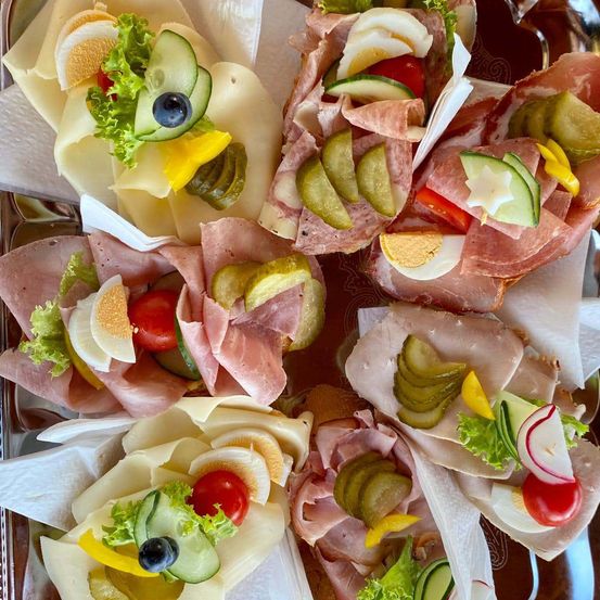 Eine Auswahl an Sandwiches mit Schinken, Käse, Gurken, Tomaten und Salat auf einem Tablett mit dekorativen Servietten.
