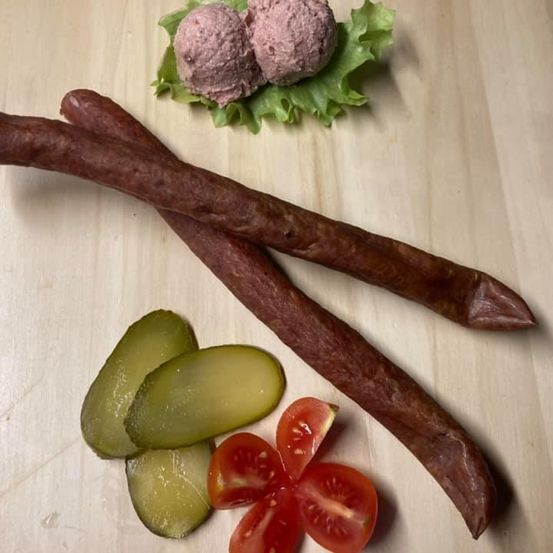 Zwei lange Würste, zwei Pickles, zwei Tomatenscheiben und zwei Fleischbällchen auf Salat auf einem Holztisch.