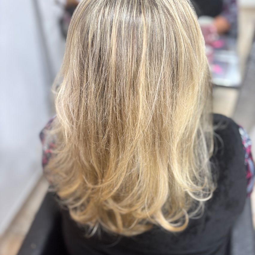 Eine Nahaufnahme einer Frau mit blondem Haar, die in einem Friseurstuhl sitzt. Die Haare sind in lockeren Wellen gestylt.