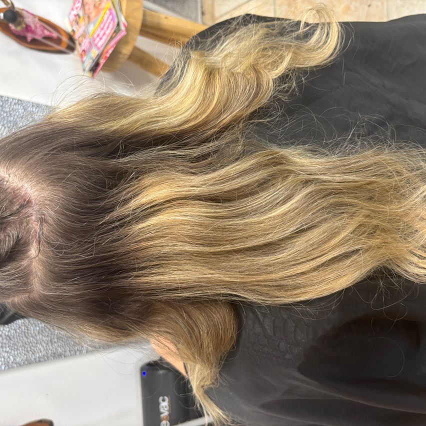 Ein Nahaufnahme von langen, welligen blonden Haaren einer Person in einer Salonumgebung. Das Haar ist in lockeren Wellen gestylt.