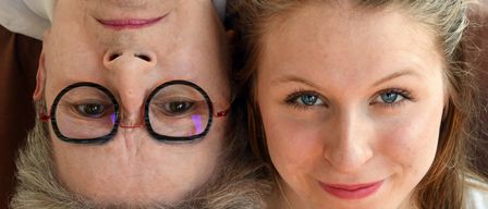 Nahaufnahme eines Frauengesichts mit Brille, das lächelt und eine jüngere Frau mit braunen Haaren und blauen Augen ansieht.