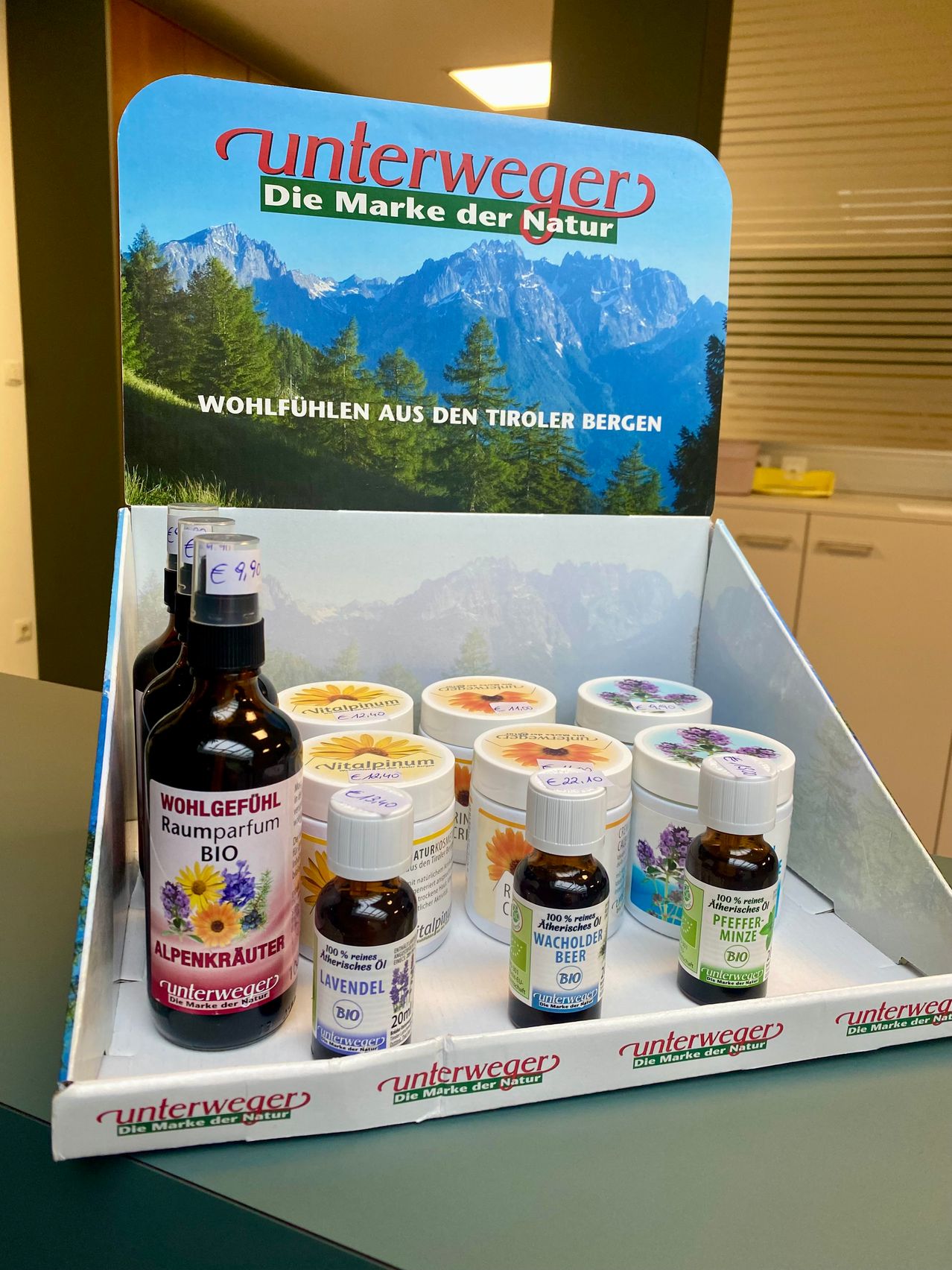 Eine Ausstellungsbox mit verschiedenen ätherischen Ölen und Extrakten von Unterweger, einer Marke aus der Region Tirol, vor einem Hintergrund von Bergen.