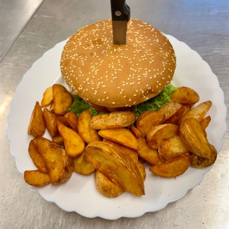 Ein Hamburger mit einem Messer darauf liegt auf einem Teller mit einer Schicht von Pommes frites.