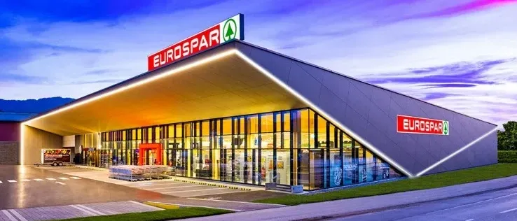 Ein EuroSpar-Geschäft mit modernem Design, nachts beleuchtet, hat eine große Glaswand und ein rotes Schild oben.