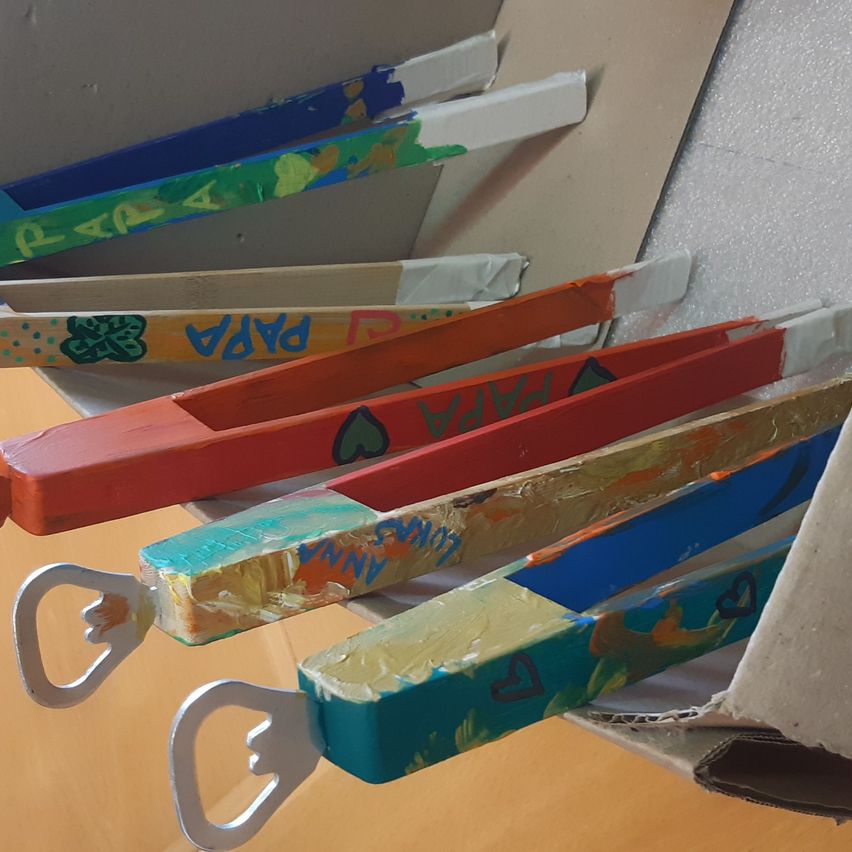 Several colorful, hand-painted wooden beer openers are arranged in a row, each with unique designs and the word PARADA written on them.
