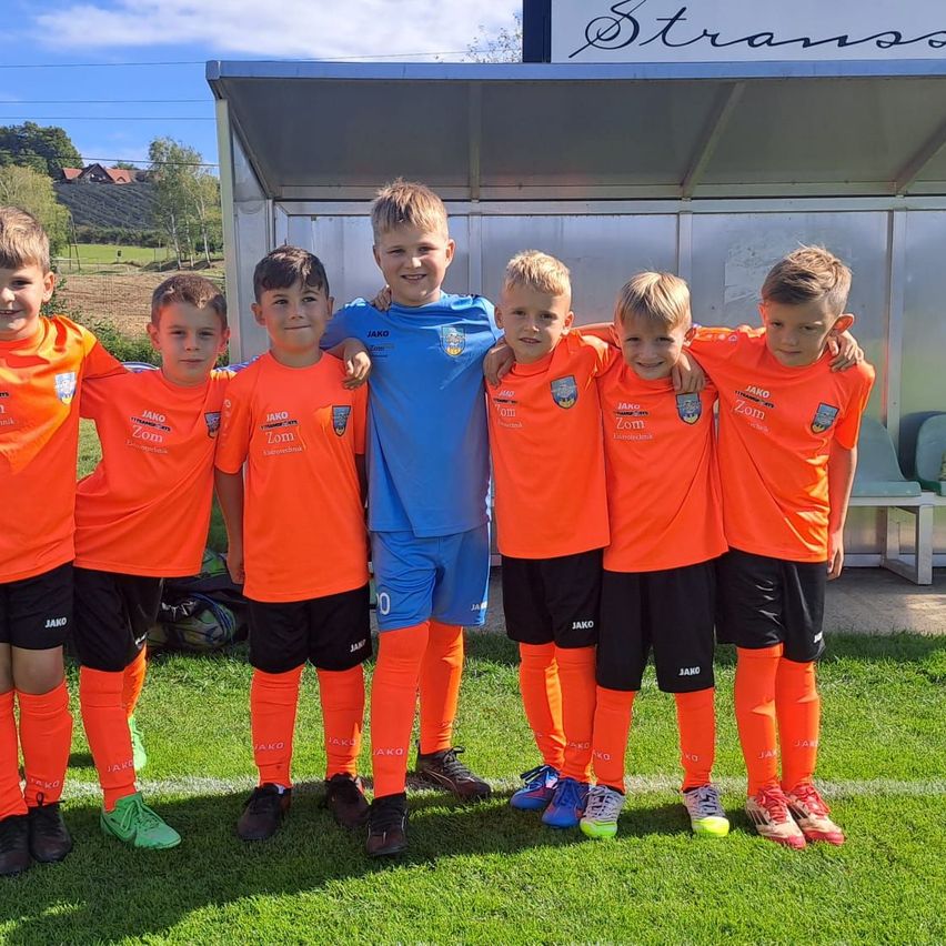 Eine Gruppe von Jungen in orangefarbenen Fußballtrikots steht auf einem Feld mit einer Bank im Hintergrund. Sie posieren für ein Foto.