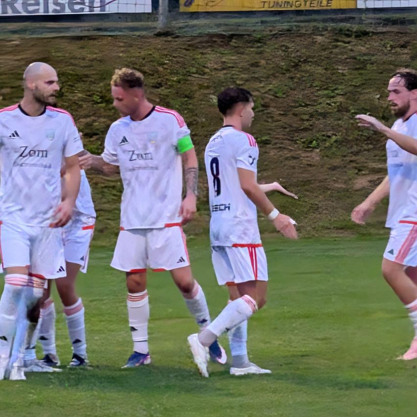Five soccer players in white uniforms with red accents are standing on a field. They are looking in different directions.