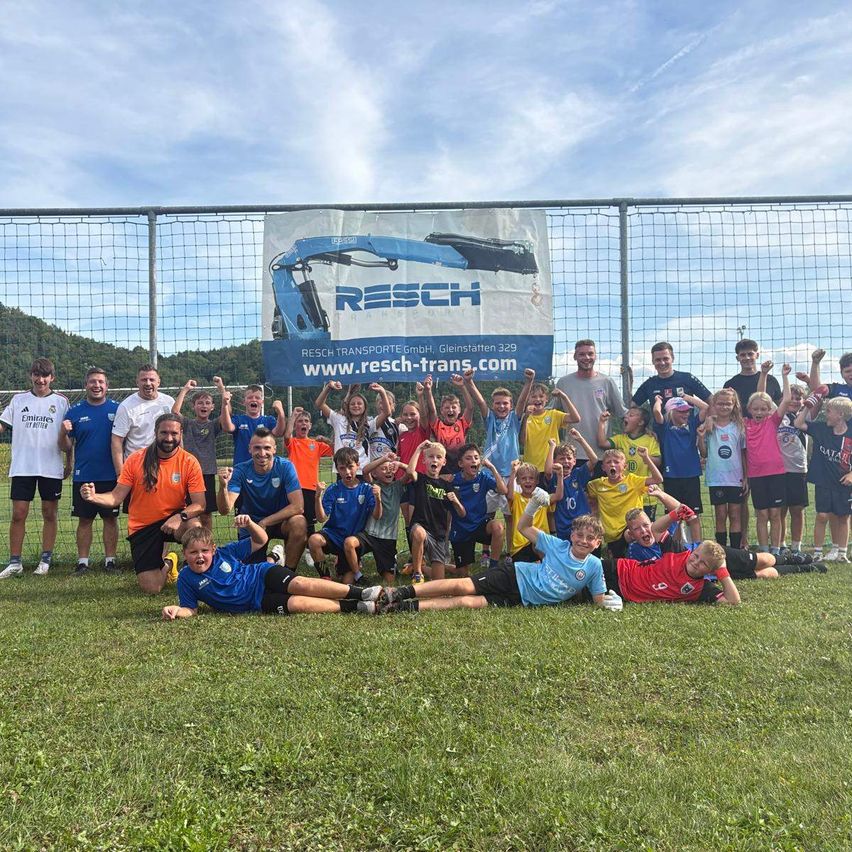 A group of soccer players and coaches pose for a photo in front of a banner.