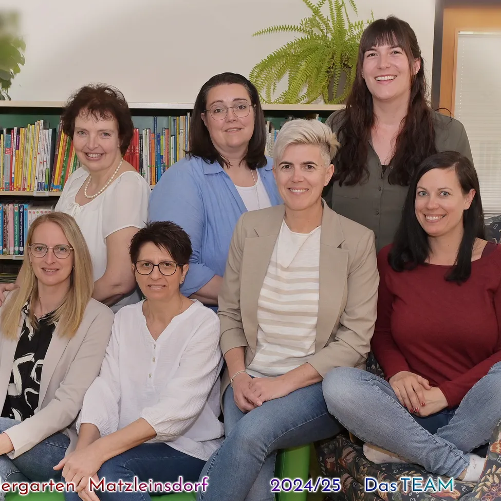 Eine Gruppe lächelnder Frauen in verschiedenen Kleidungsstücken sitzt in einem Raum, möglicherweise einer Bibliothek, mit Büchern an den Regalen im Hintergrund. Das Bild hat einen Wasserzeichen des Jahres 2024/25.