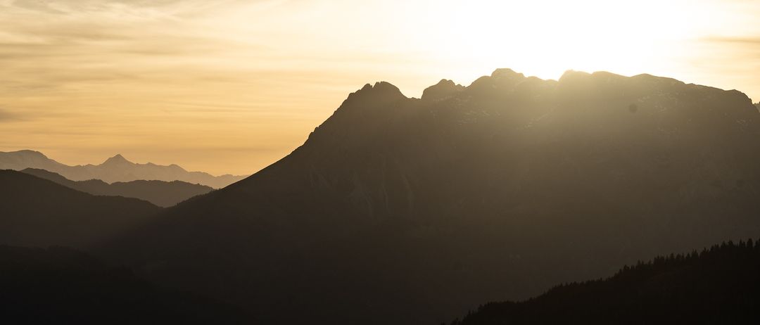 Eine Silhouette von Bergen unter einem goldenen Sonnenuntergang mit klarem Himmel und verstreuten Wolken.