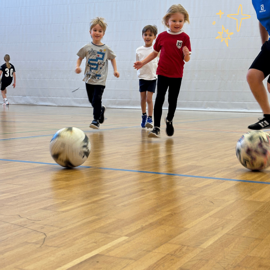 Kinder rennen auf einem Holzboden mit zwei Fußballbällen auf beiden Seiten. Ein Kind ist in einem roten Shirt und ein anderes in einem weißen Shirt.